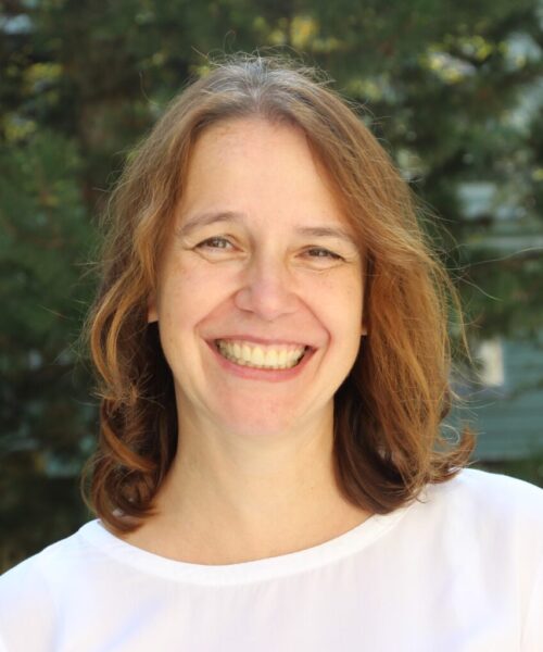 headshot of katarina krizkova smiling in a white shirt with green trees behind her