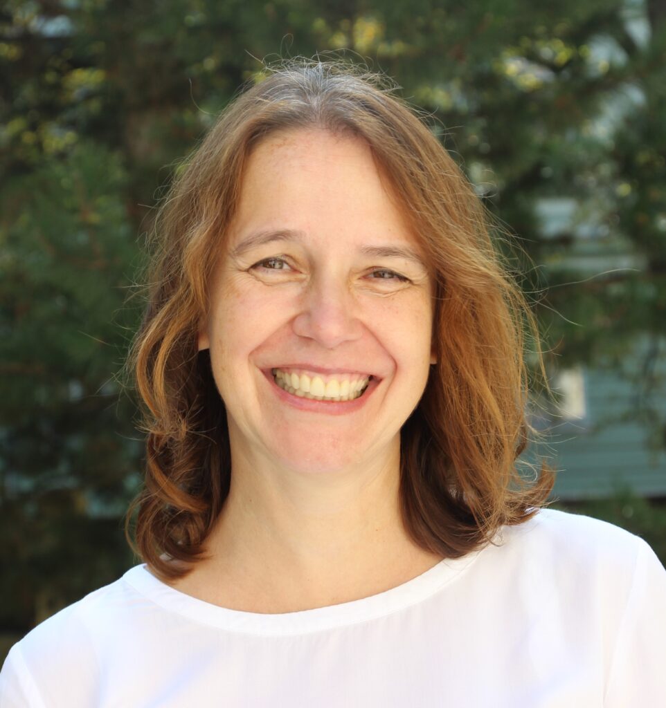 headshot of katarina krizkova smiling in a white shirt with green trees behind her